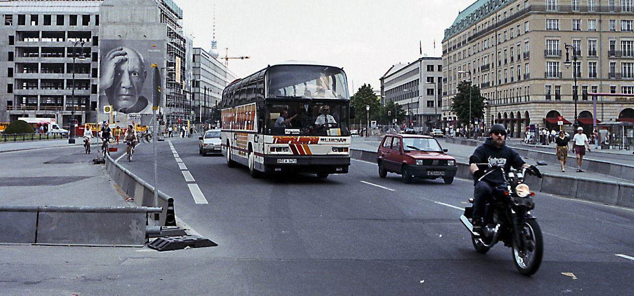 Etualalla moottoripyöräilijä ja linja-auto, taustalla iso seinäkuva Pablo Picassosta.