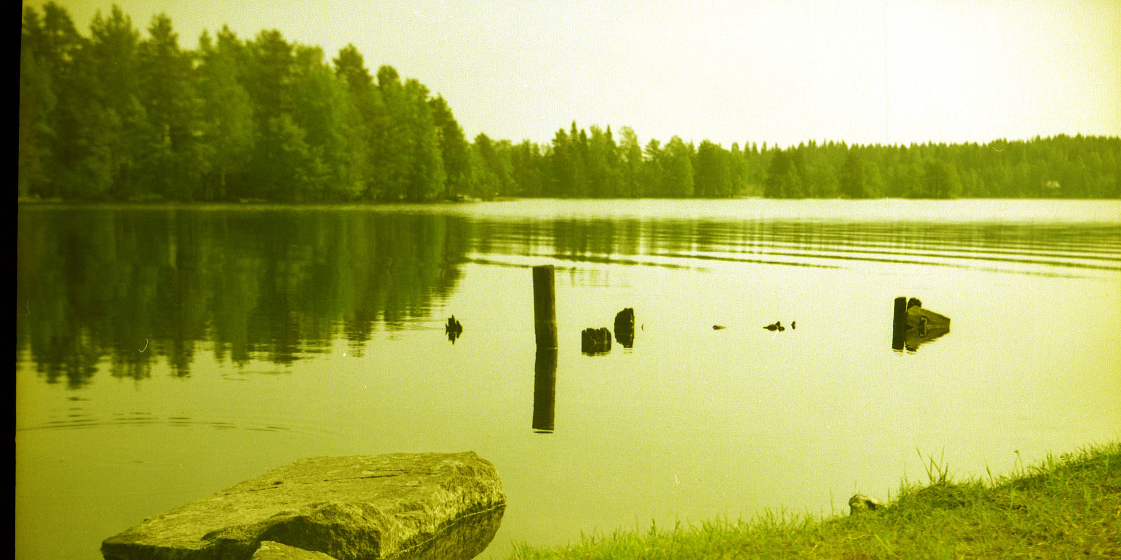 Maisemapanoraama, jossa järvenrantaa ja rantakiviä, vastaranta näkyy hyvin.